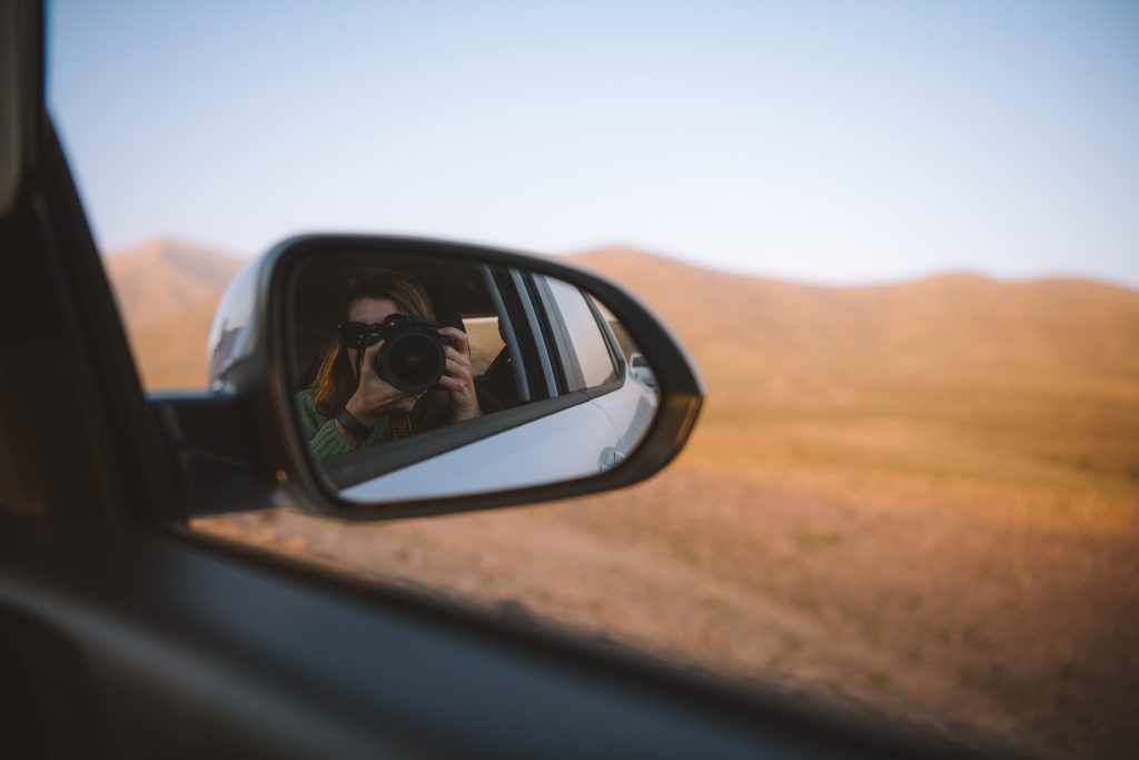 self portrait of kelly in side view mirror of rental car