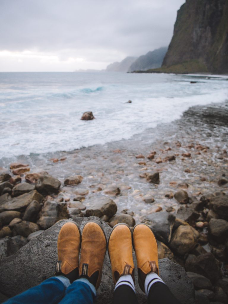 couple's blundstone shoes with the ocean and cliffs in the background