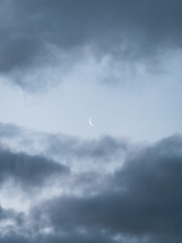 waning crescent moon with clouds in a blue sky