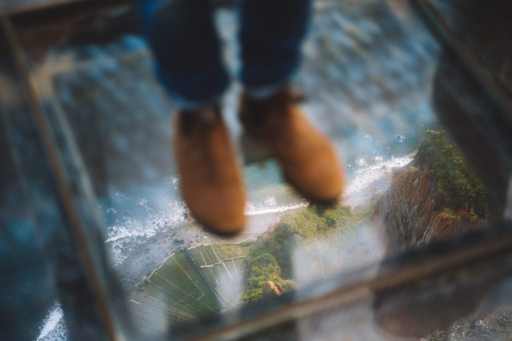 florian's shoes while standing on a glass platform looking down at the ocean and fields