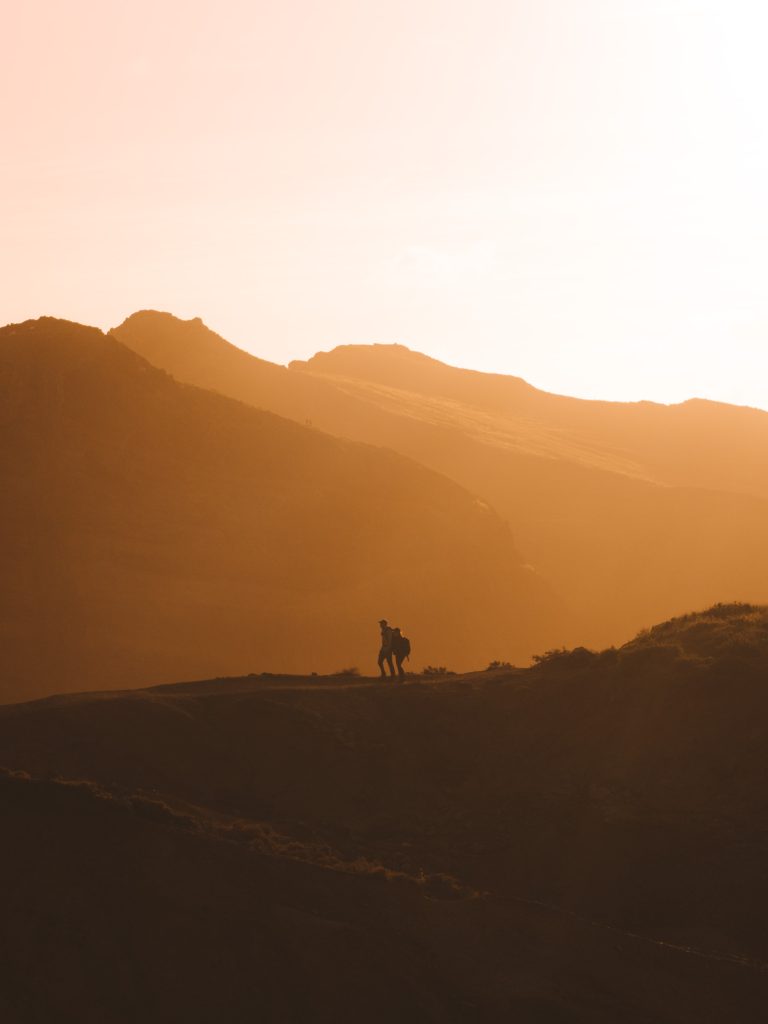 couple walking on a mountain with the sun coming up over it