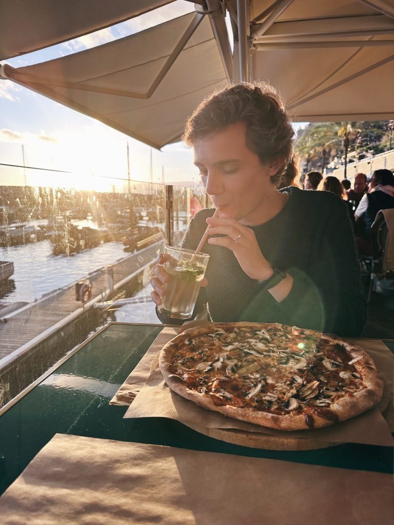 florian drinking ice tea with a mushroom pizza before him on the table next to the harbour in calheta madeira