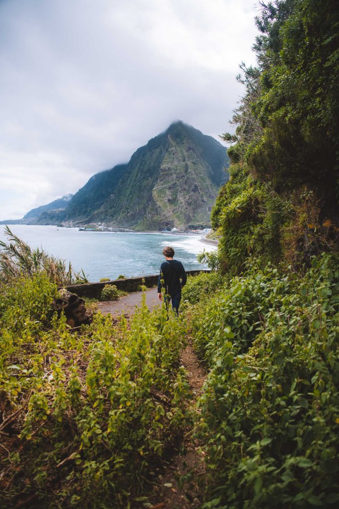 florian walking on a deserted road overgrown with weeds with cliffs and the ocean in the background