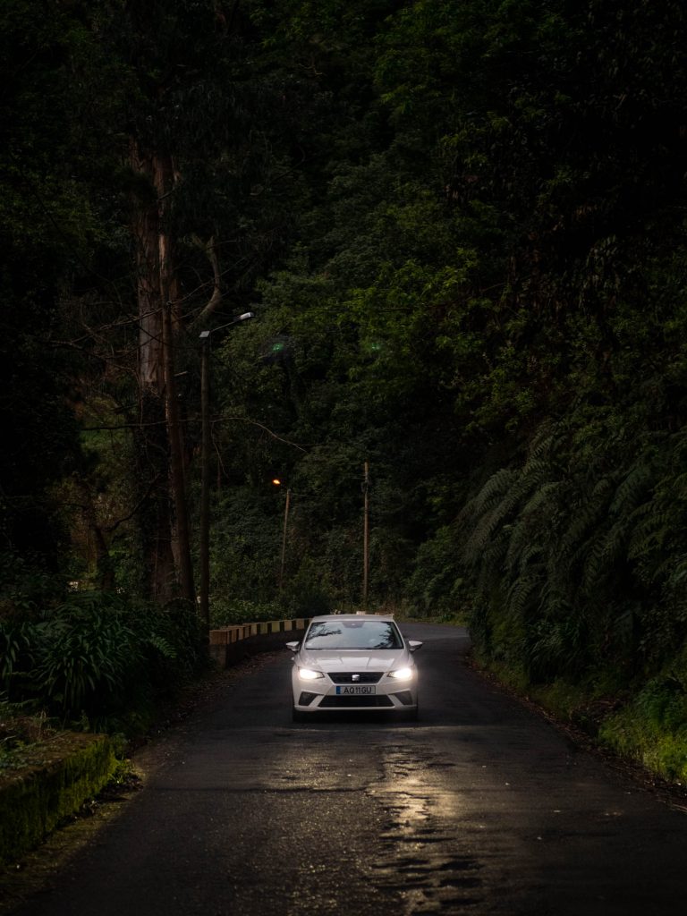 white rental car with the lights on in the middle of the road in the evening