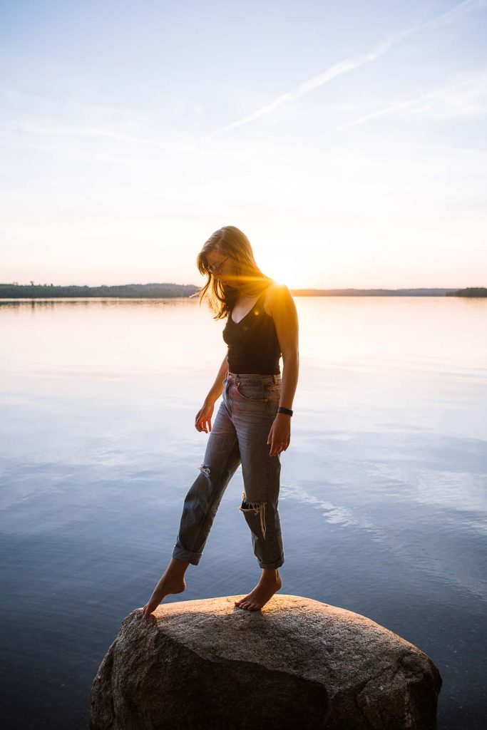 kelly posing on a rock in the lake with the sun setting behind her in sweden