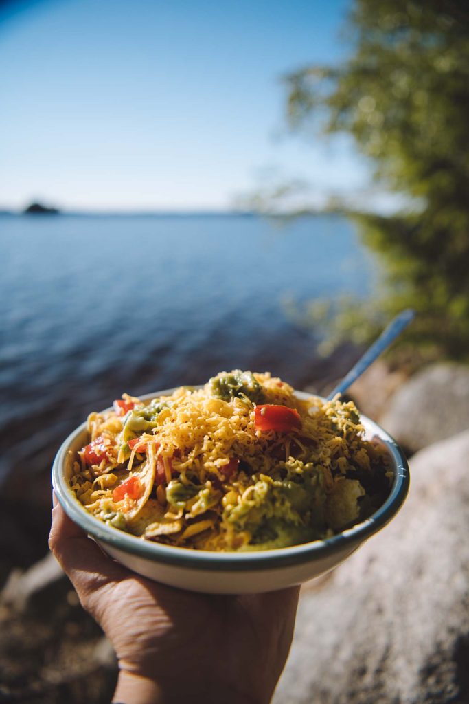 a plate of nachos with shredded cheddar with a view of a lake behind