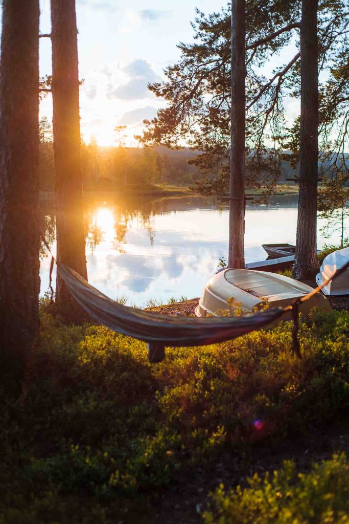 sunset over the water seen from behind a hammock hanging between the trees with boats in the background