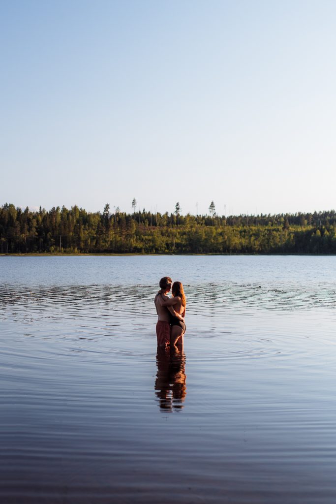 me and florian hugging while watching the sunset standing knee deep in the water of a lake with trees in the background