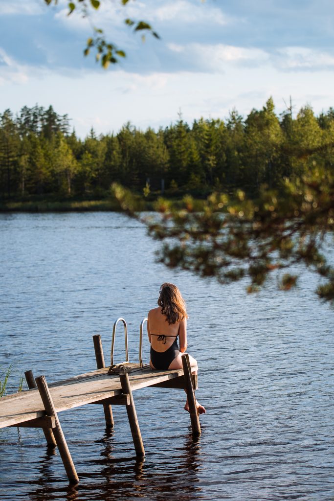 kelly in her bathing suit sitting on a wooden jetty with her feet dangling over the water of the lake